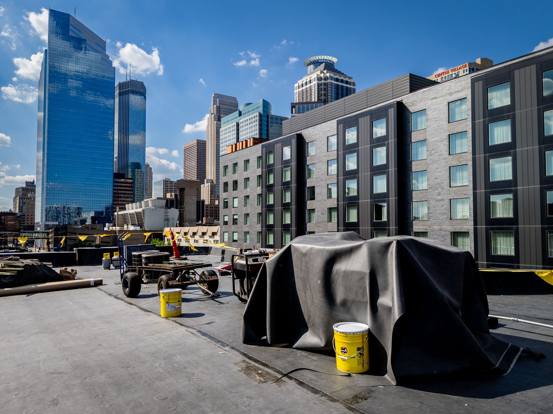 City construction site with covered equipment, yellow buckets, and modern buildings under a blue sky