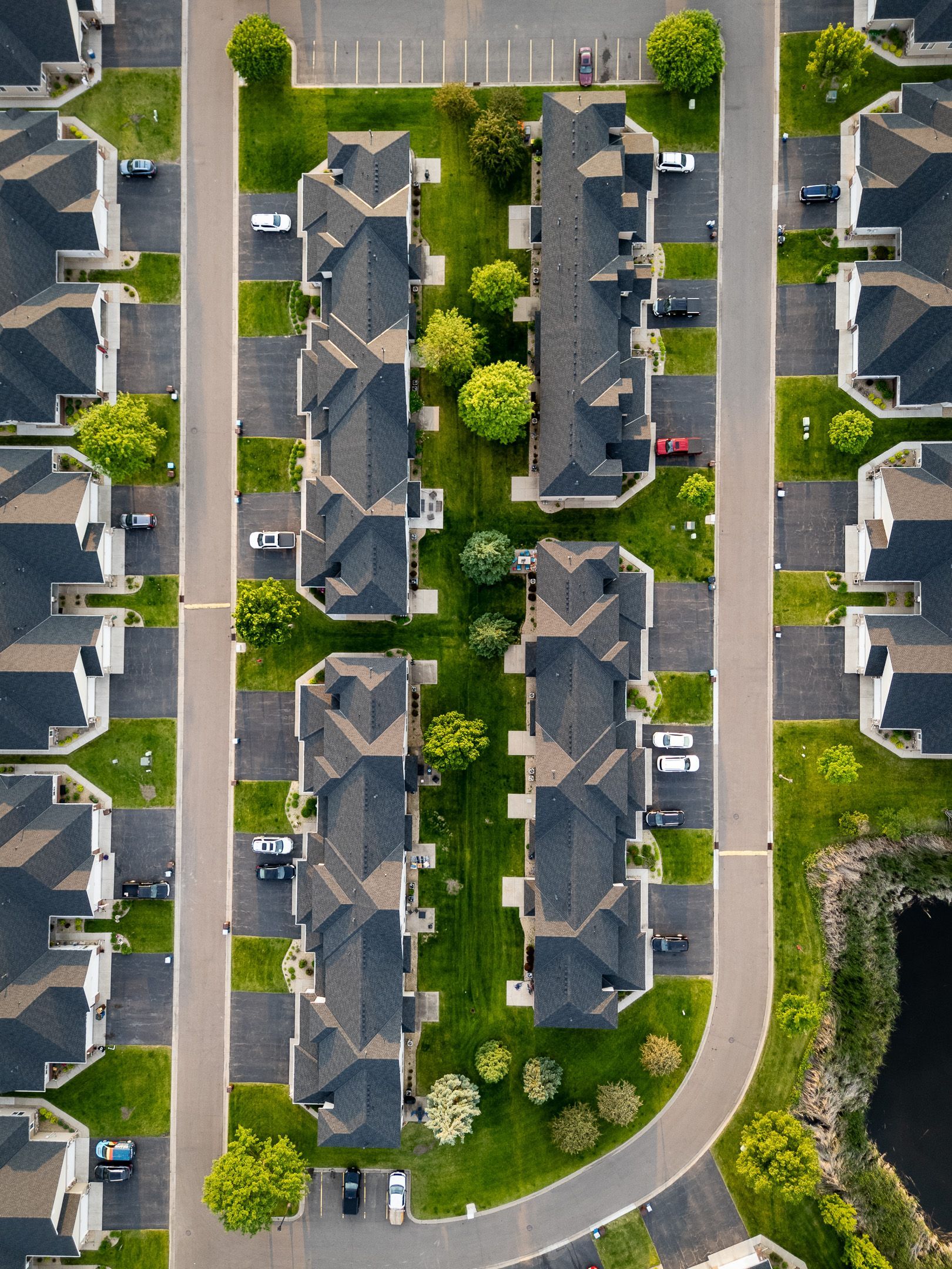 Aerial view of a suburban apartment complex with gray roofs, parked cars, and tree-lined roads