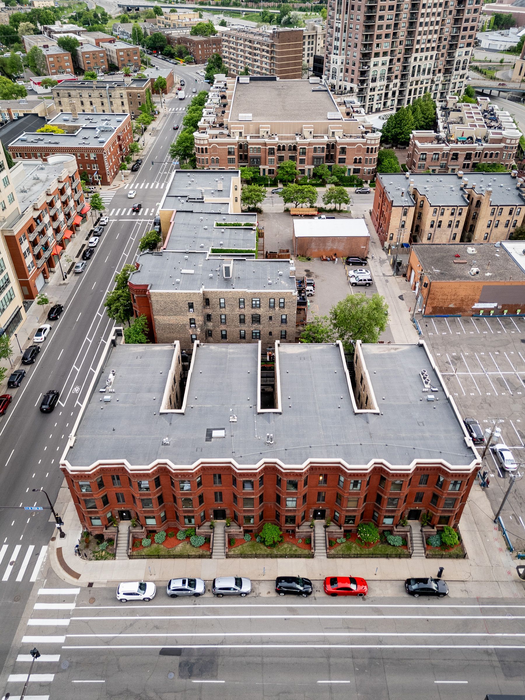 Aerial view of a city block with brick buildings, parked cars, and tree-lined streets.
