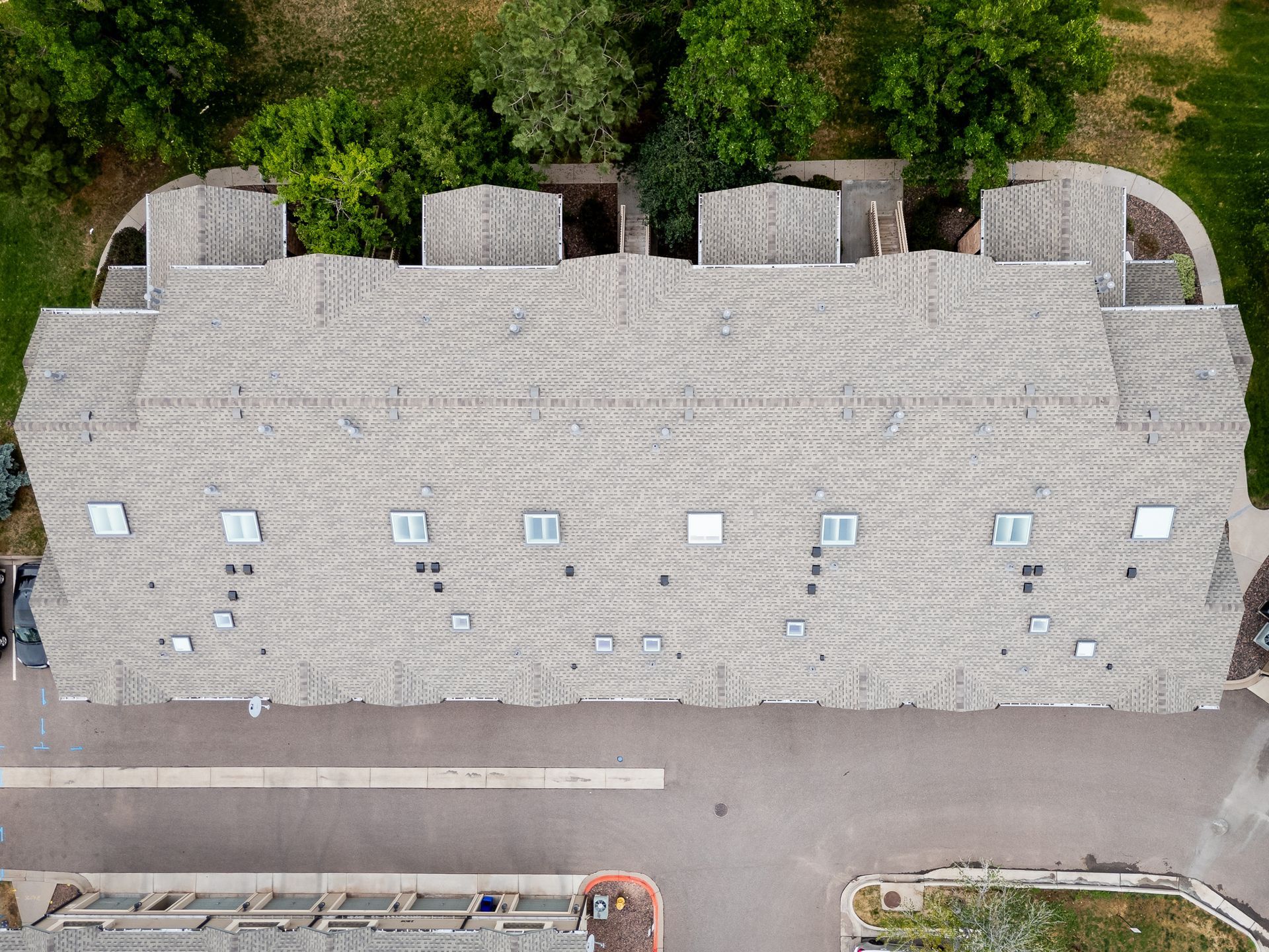 Aerial view of a long stone building with small windows beside a road and trees.