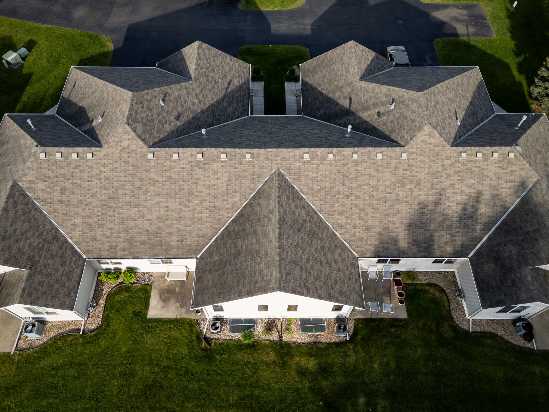 Aerial view of a large beige roof with multiple gables and dormers, surrounded by green lawns and driveway.