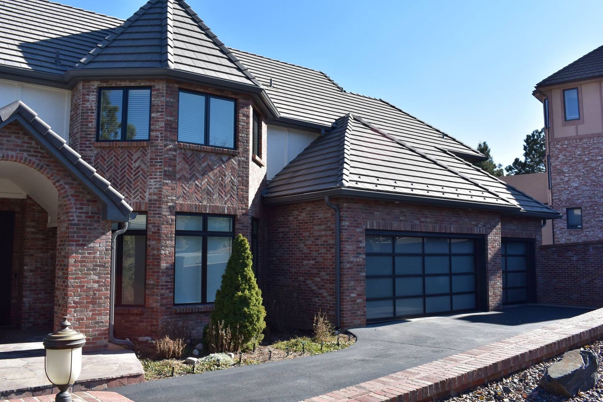 Brick two-story house with dark garage doors, arched windows, and a tiled roof in bright daylight