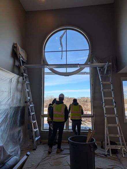 Two workers in safety vests stand inside a room with a large round window under renovation.