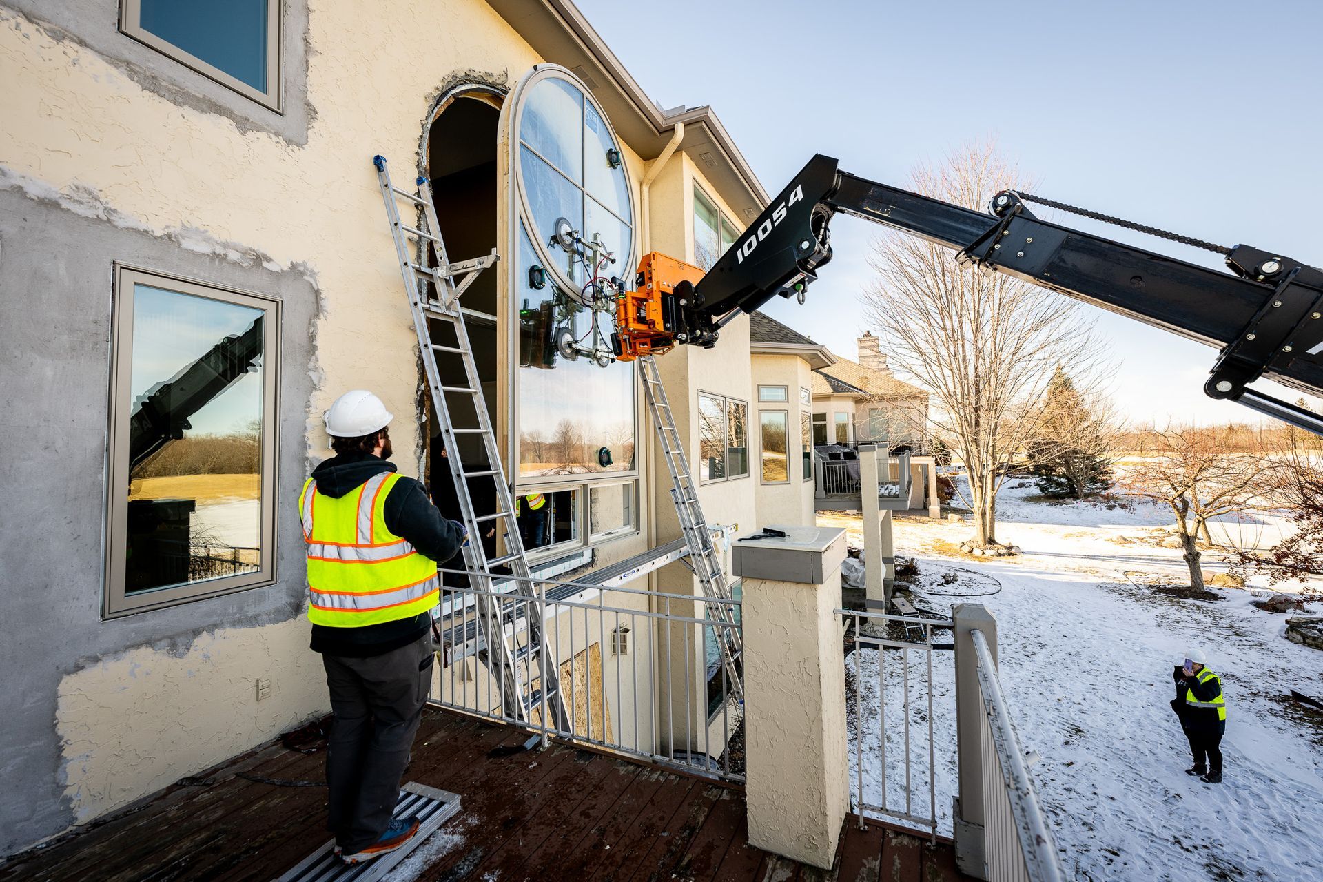 Workers using a crane to remove a large window from a house in winter