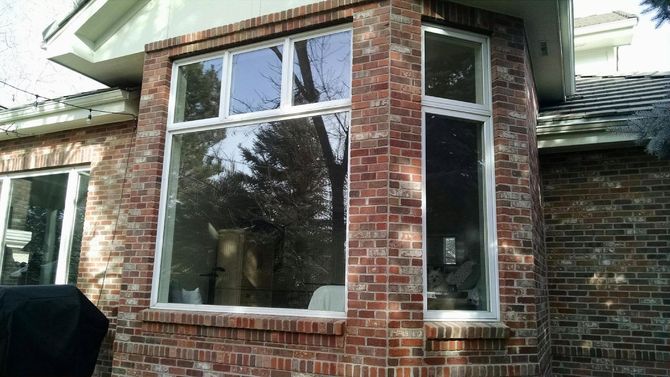 Brick house exterior with large white-trimmed window and a narrow side window under the roof eave