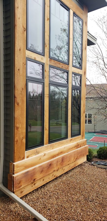 Wooden-framed glass doors and windows on a modern cabin exterior, with gravel and a potted plant nearby