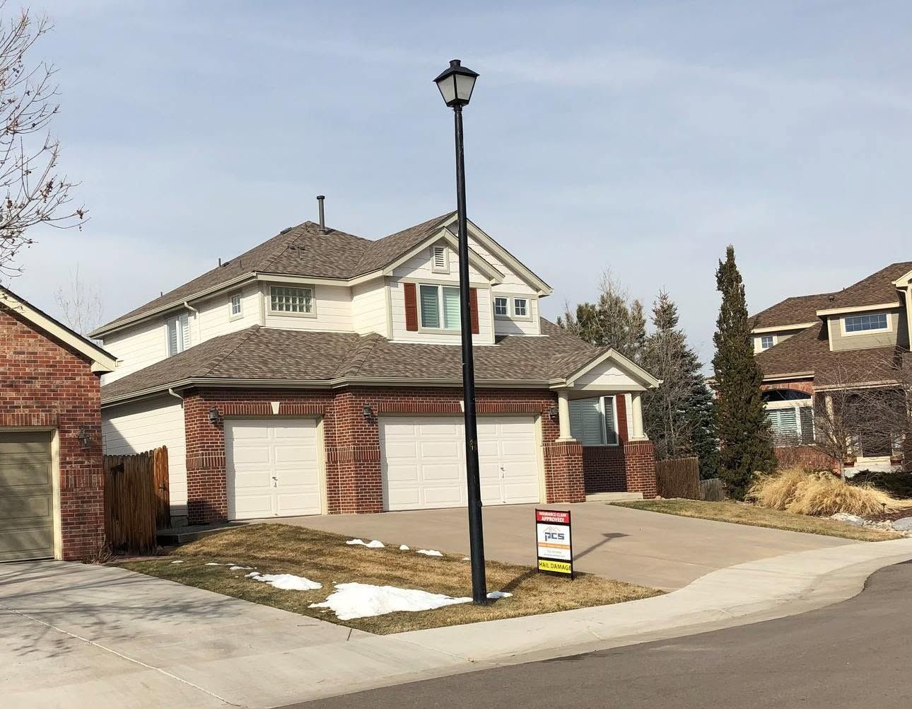 Suburban two-story house with three-car garage, lamp post, and a small snow-covered lawn.