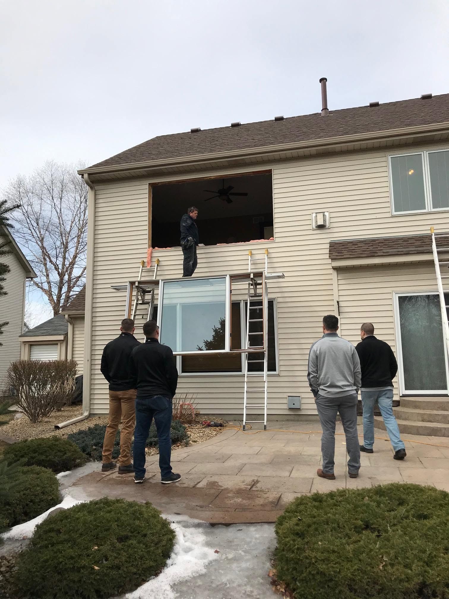Workers on ladders repairing the upper front of a beige two-story house