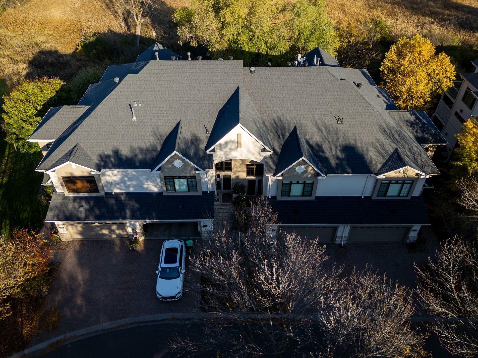 Aerial view of a gray-roofed house with a white car parked in the driveway, surrounded by trees.