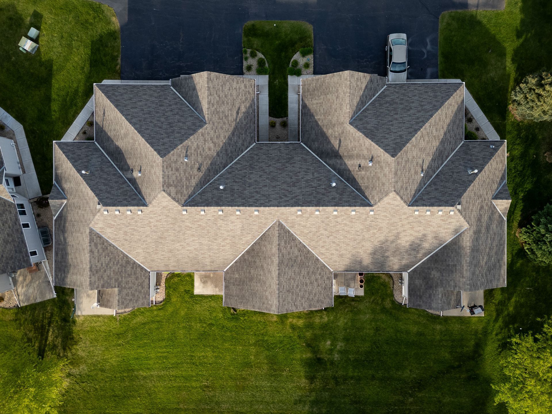 Aerial view of a large gray-roofed suburban house with a green lawn and driveway.