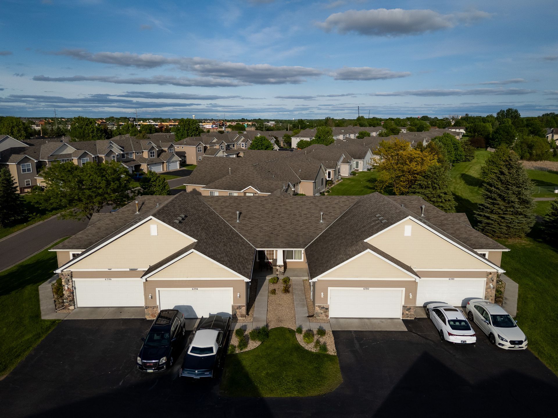 Suburban duplex homes with two driveways and parked cars under a partly cloudy sky