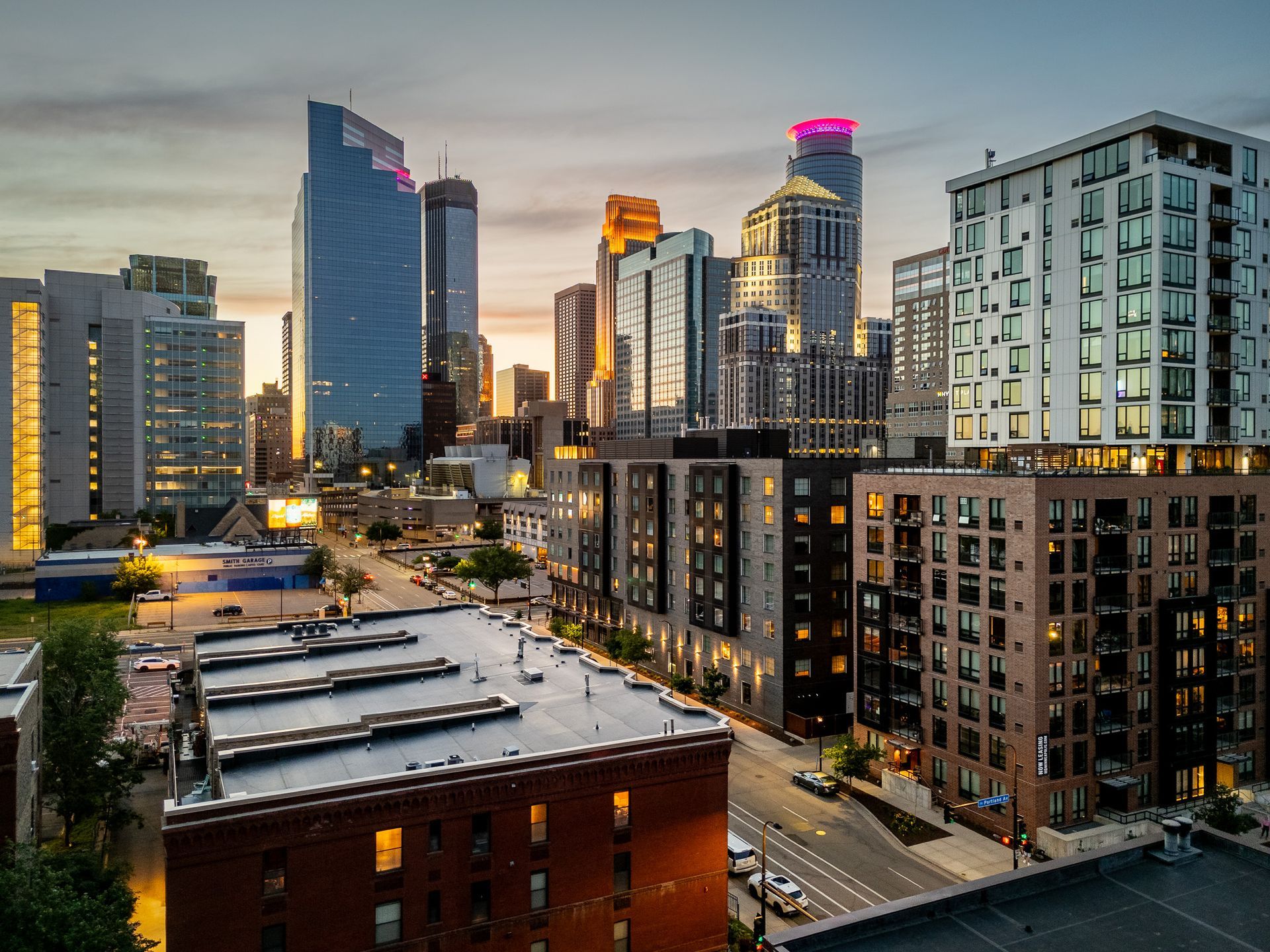 City skyline at dusk with lit high-rises and brick rooftops in the foreground