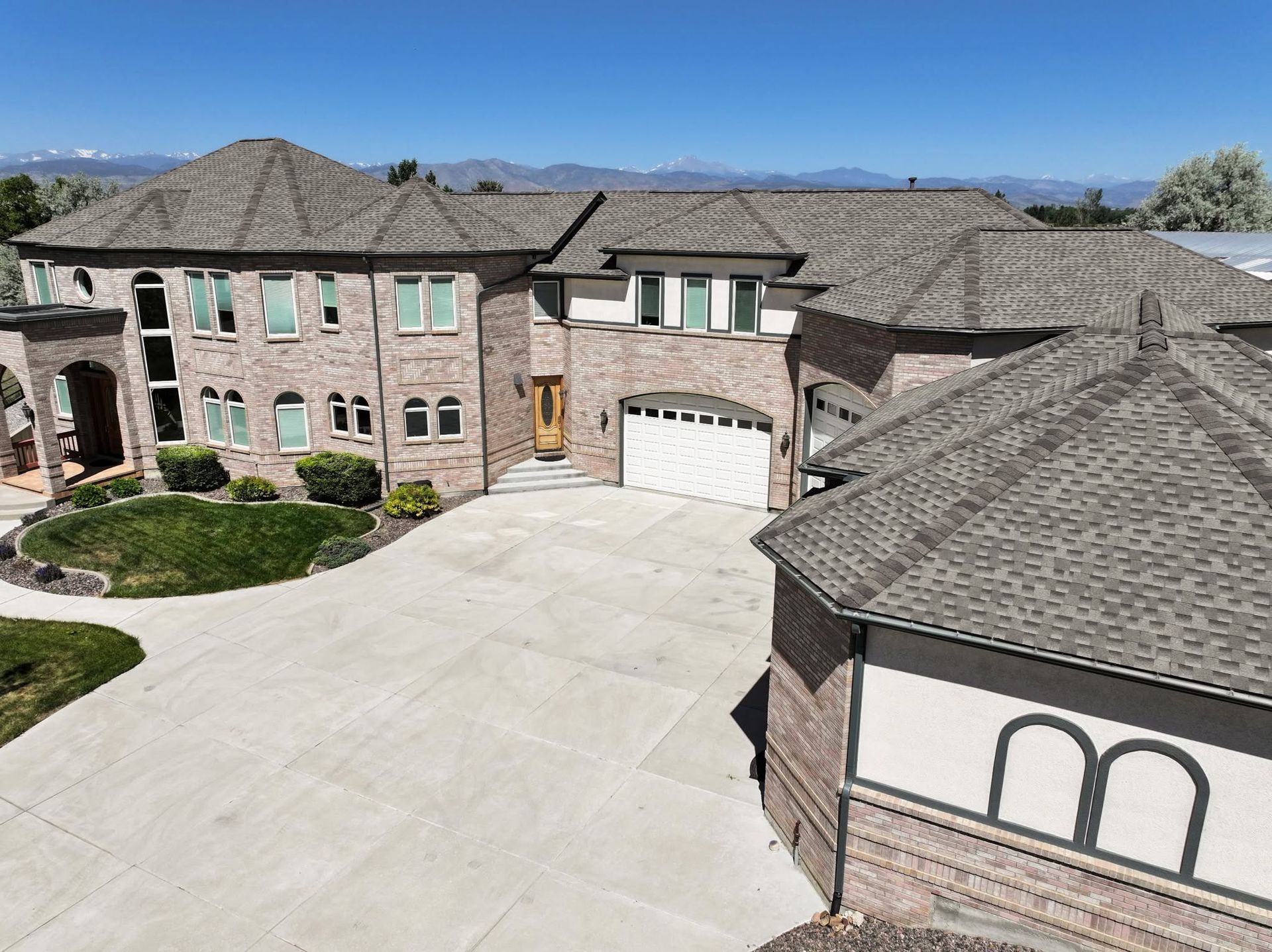 Large brick mansion with a wide driveway, two-story facade, and tiled roof under a clear blue sky