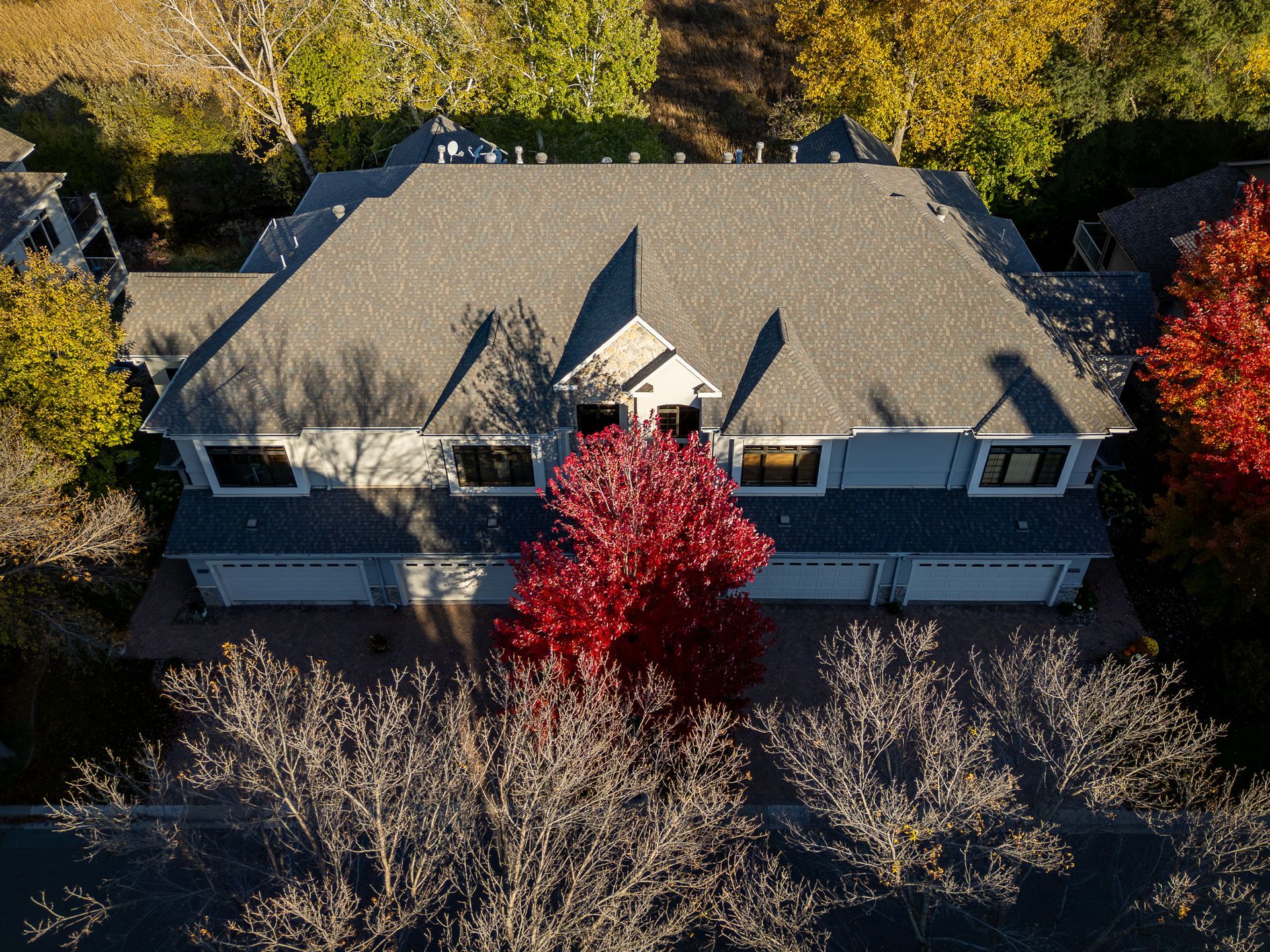 Aerial view of a gray-roofed house surrounded by autumn trees, including a bright red tree in front.