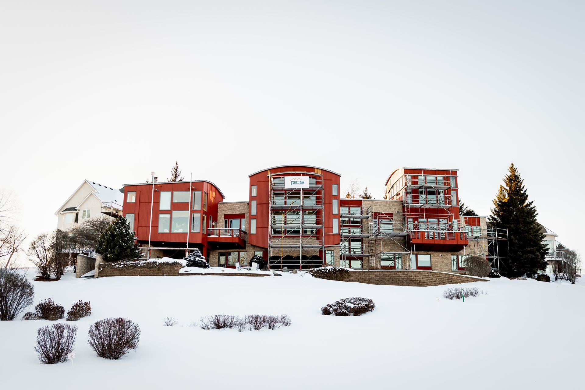 Red apartment buildings on a snowy hillside with trees and shrubs in winter landscape