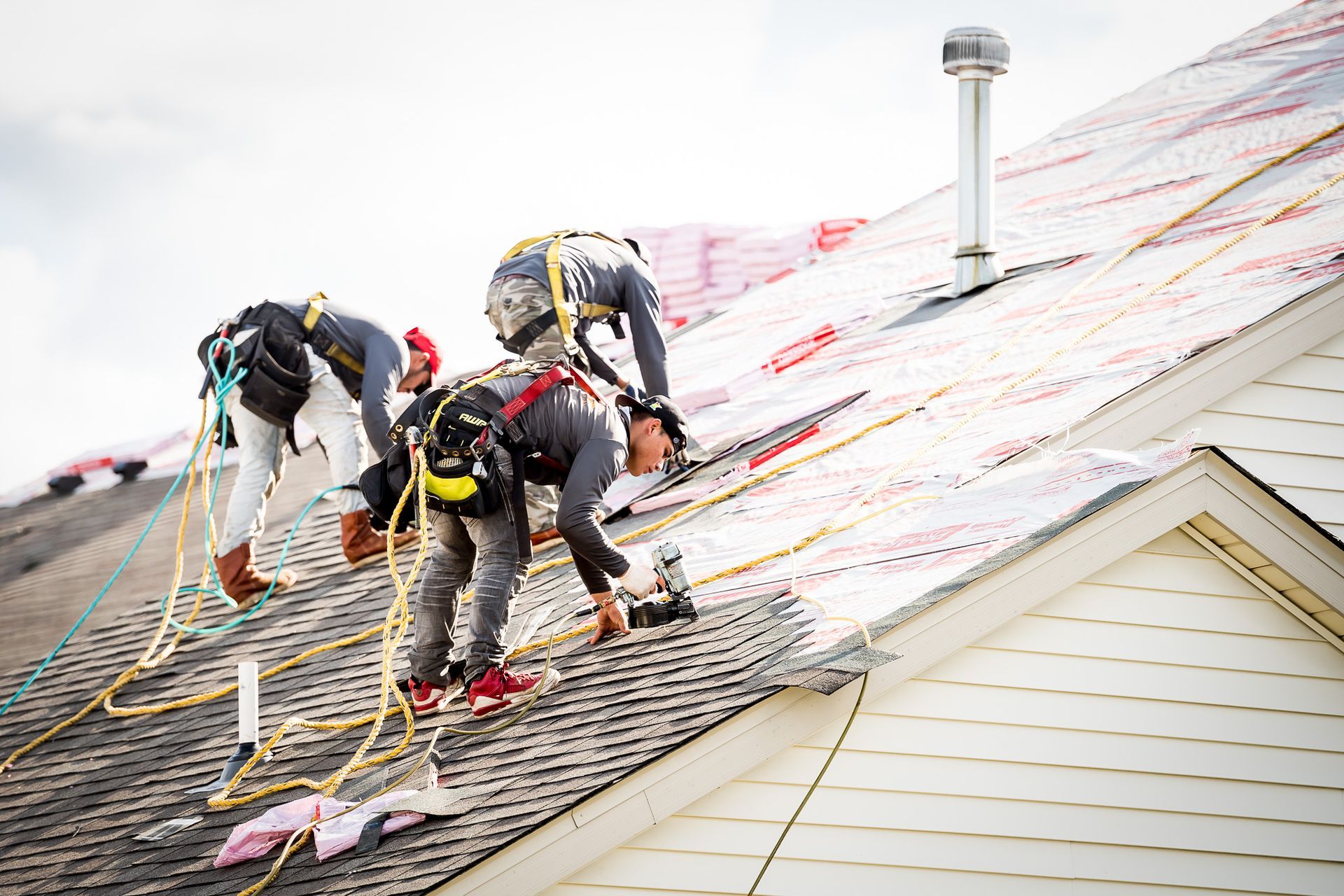 Roofers working on a steep roof covered with protective netting and safety ropes
