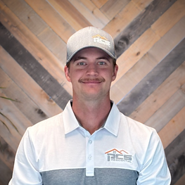 Man in gray cap and white polo shirt standing before a wood chevron wall