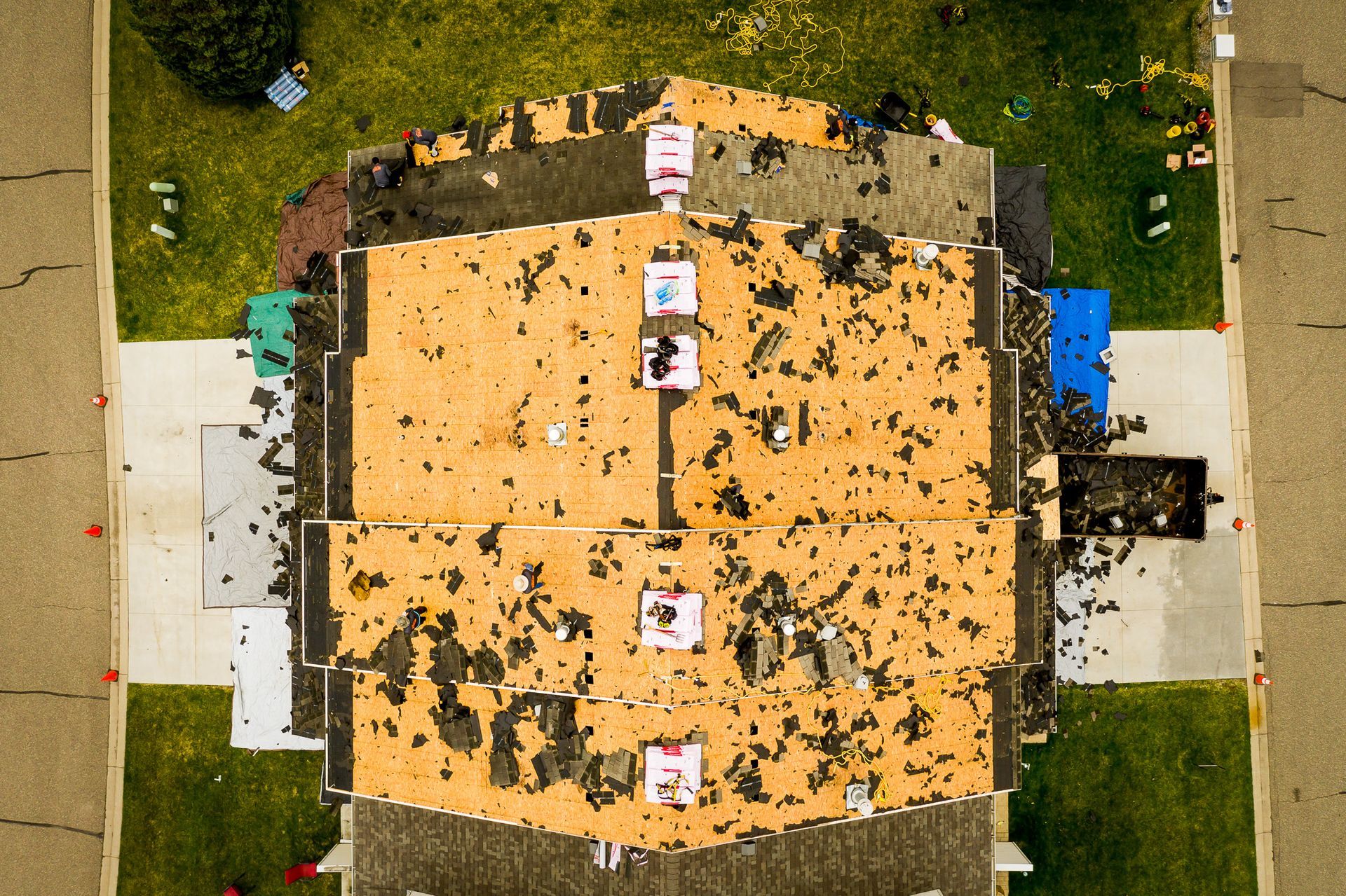 Aerial view of a brown-roofed house with a tan center roof, surrounded by green lawn and scattered leaves.
