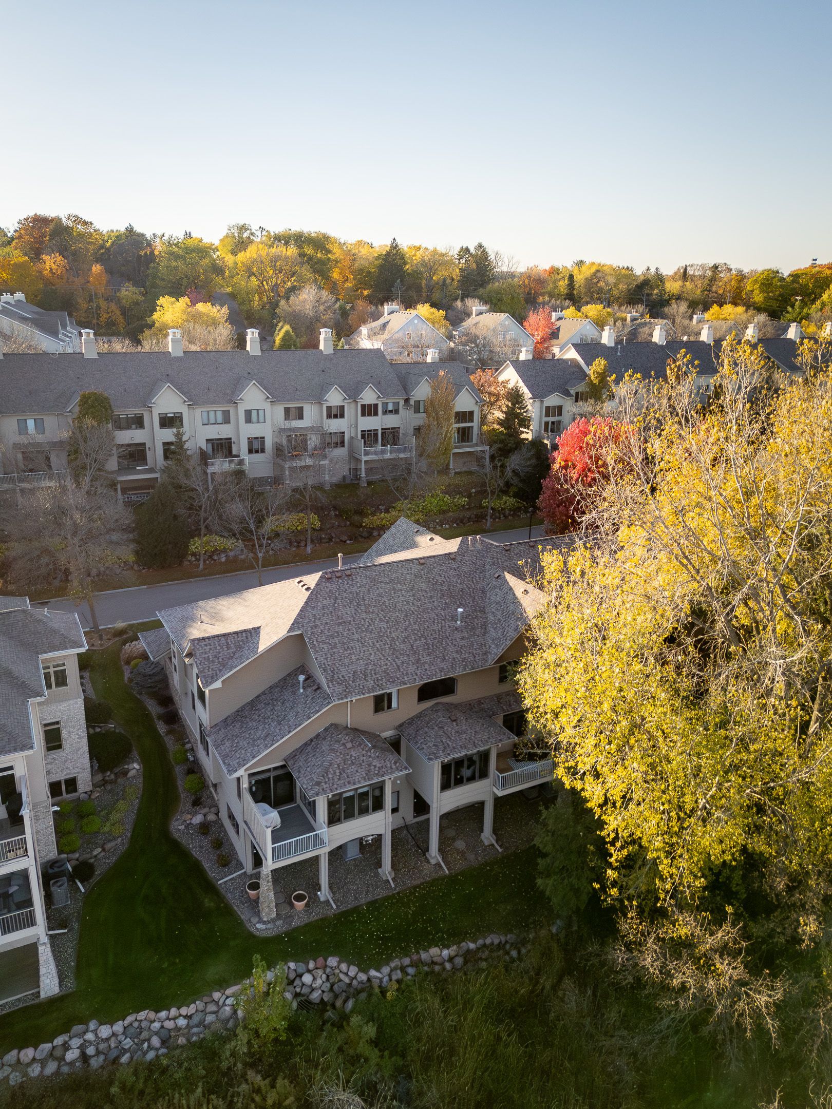 Aerial view of a neighborhood with houses, autumn trees, and a large building at sunset