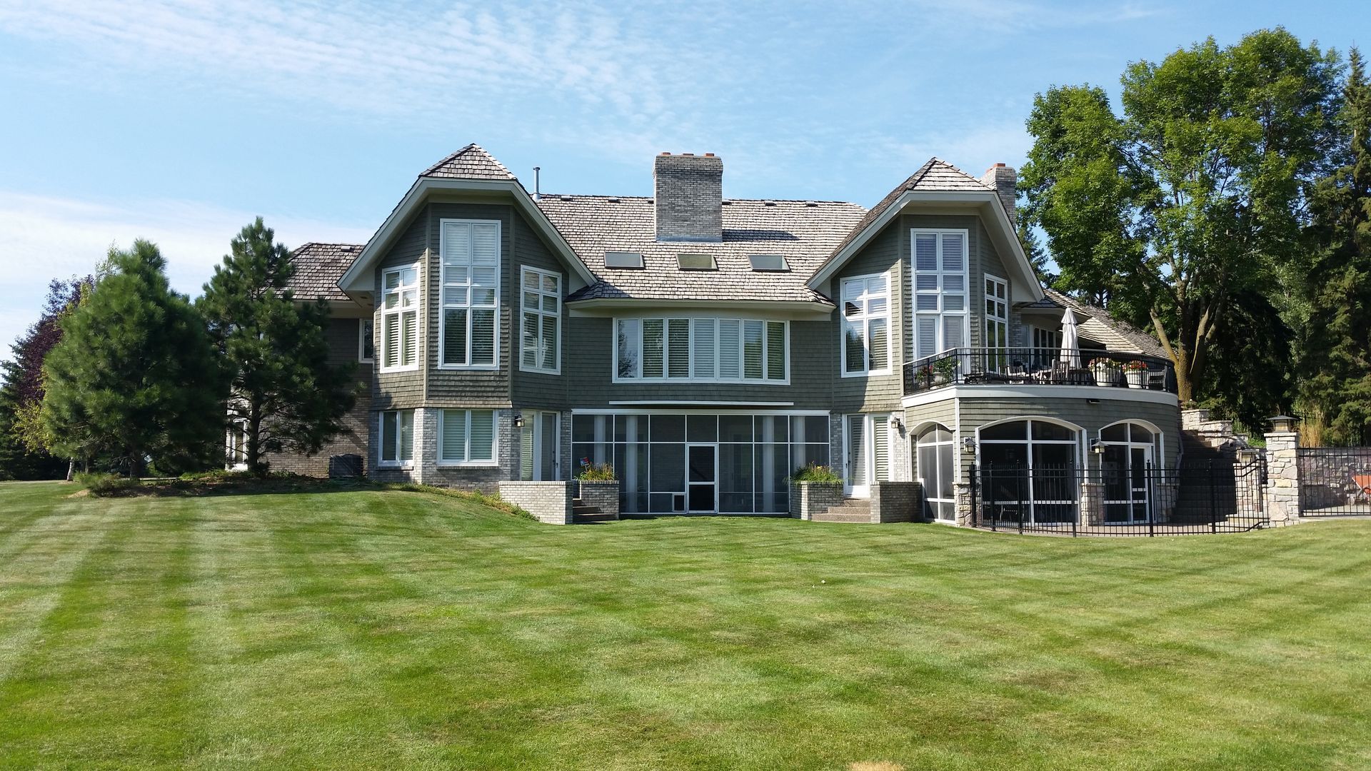 Large gray stone house with white trim and a broad green lawn under a clear blue sky