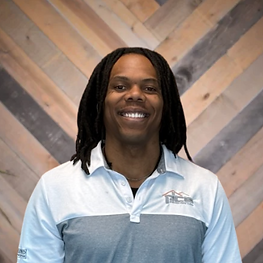 Smiling person in a light blue collared shirt standing before a wood-patterned wall