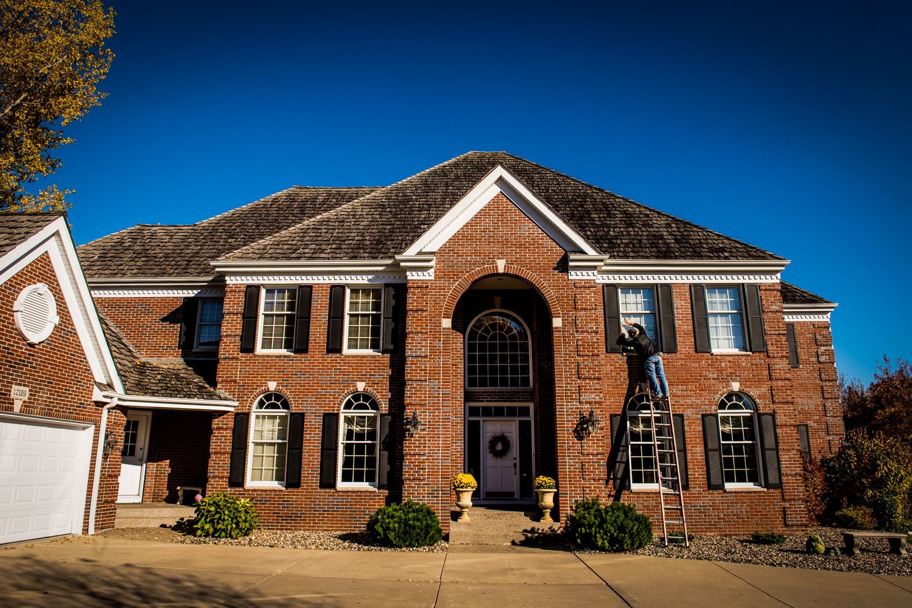 Brick suburban house with white trim, arched entry, and two-story windows under a blue sky