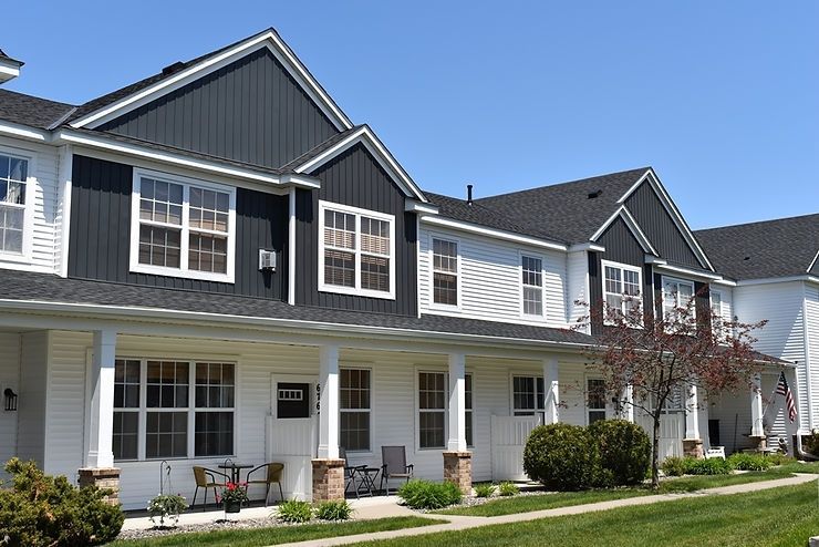 Row of modern suburban townhouses with white porches and dark gray siding under a blue sky