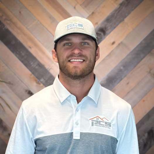 Smiling man in a white and blue polo and beige cap standing in front of a wood-patterned wall