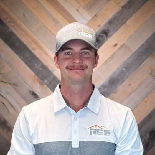 Man smiling in a gray cap and white polo against a wood plank wall