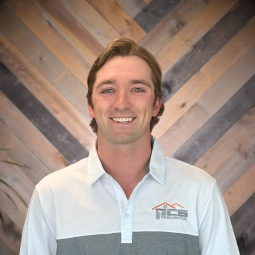 Smiling person in a white and gray collared shirt against a wood chevron wall