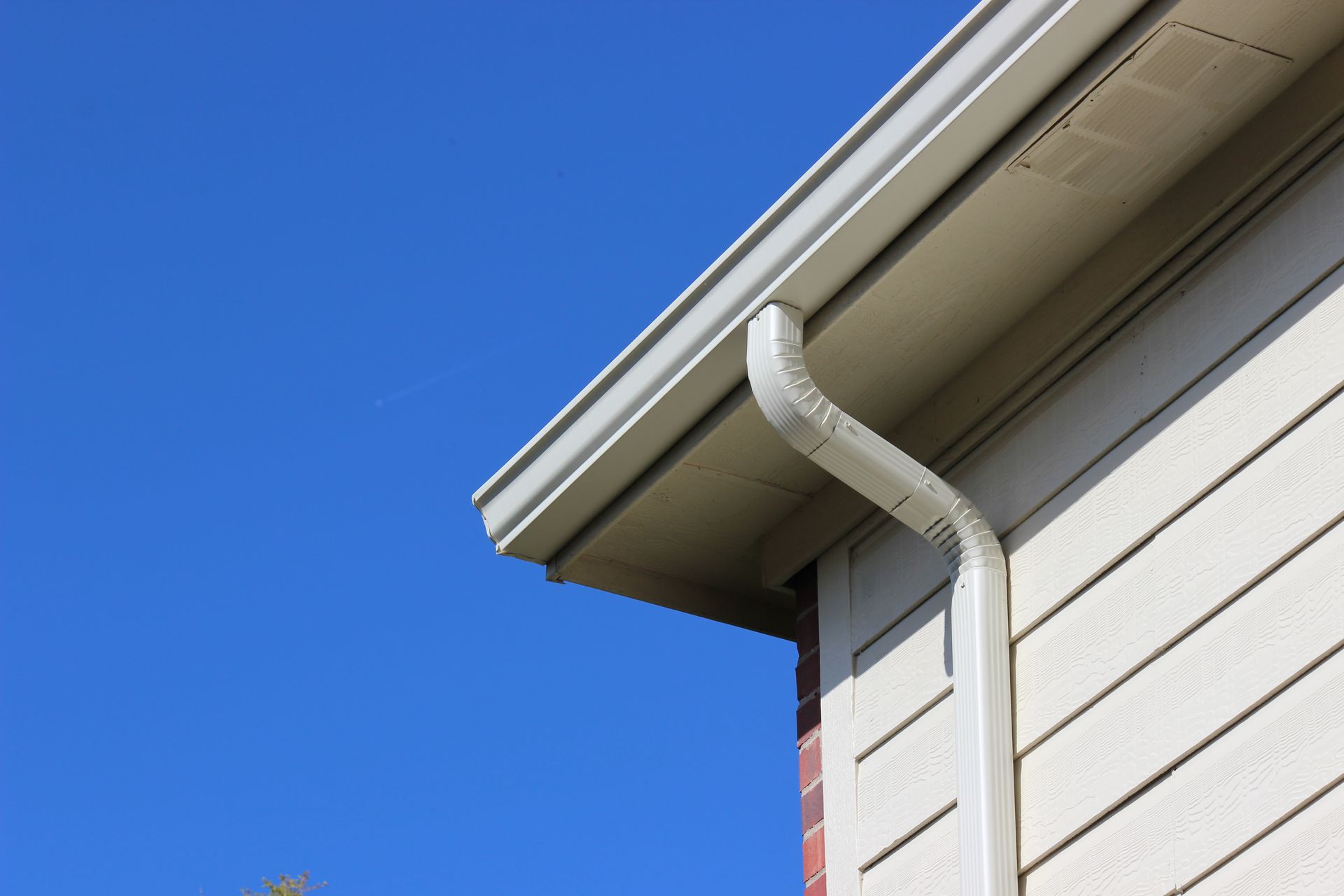 White house corner with gutter and downspout against a clear blue sky