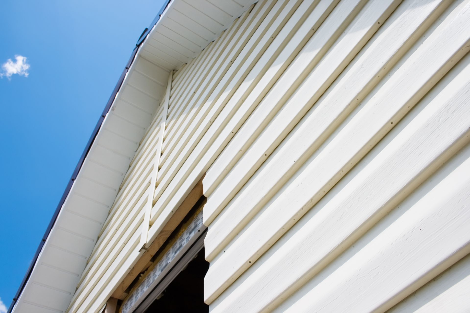 White house siding and roofline against a blue sky, with a window opening below