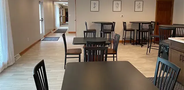 Empty dining room with black tables and chairs along a beige hallway
