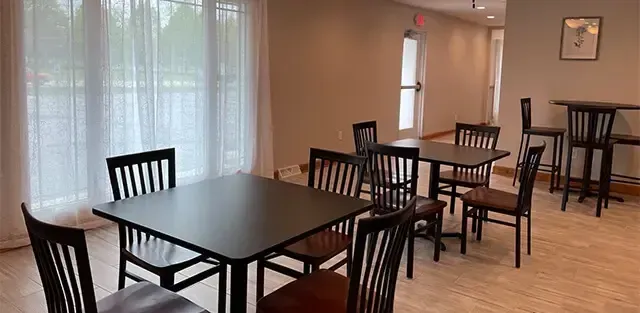 Empty dining area with dark wooden tables and chairs near a bright window