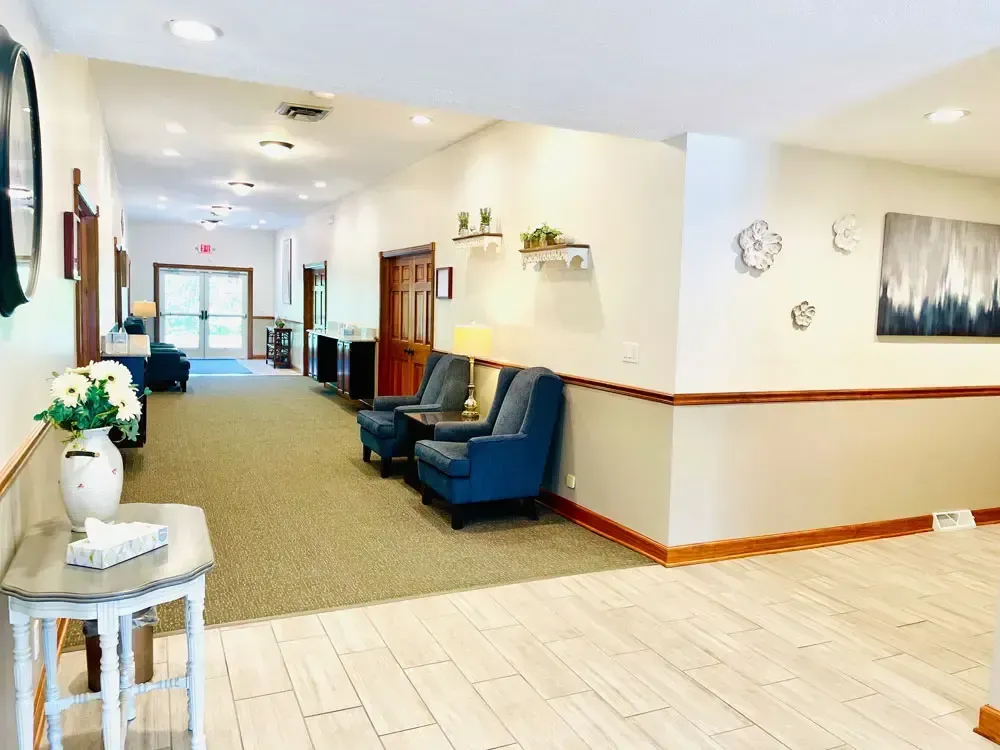 Bright hallway with blue chairs, wall art, and tiled flooring in a clean residential or care facility.
