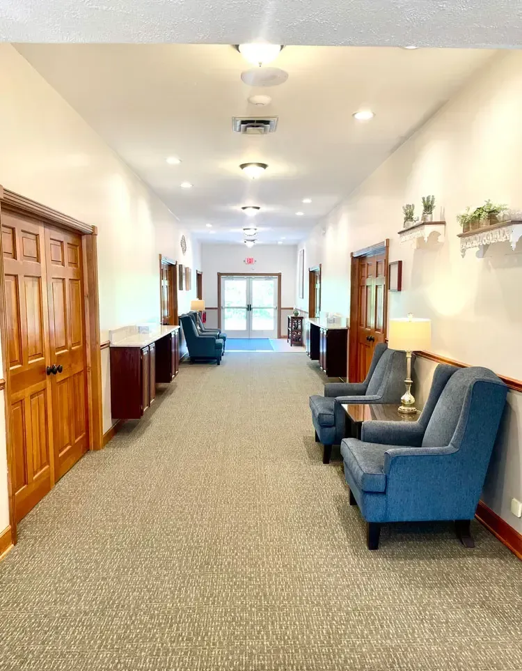Bright hallway with blue chairs, wood doors, and carpeted floor in a quiet building lobby