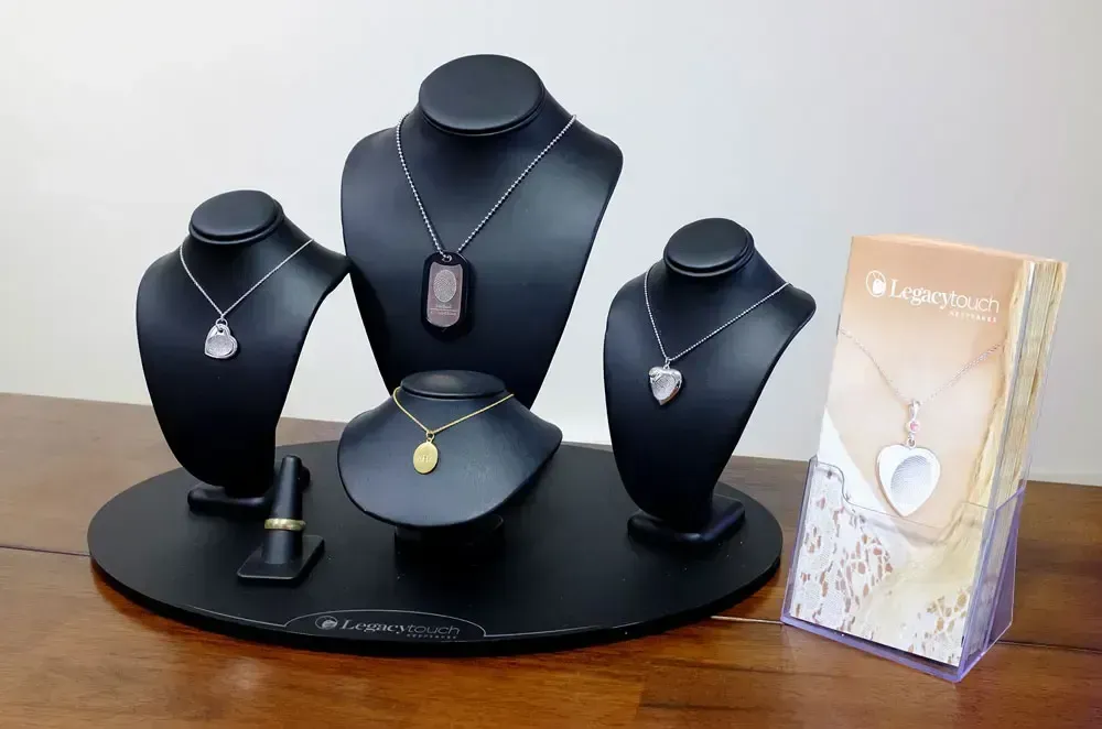 Jewelry display with black bust stands and necklace pendants beside a boxed pendant on a table