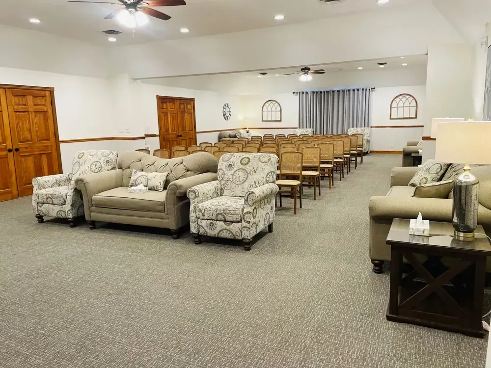 Spacious meeting hall with patterned sofas in front and rows of tan chairs under ceiling fans and lights