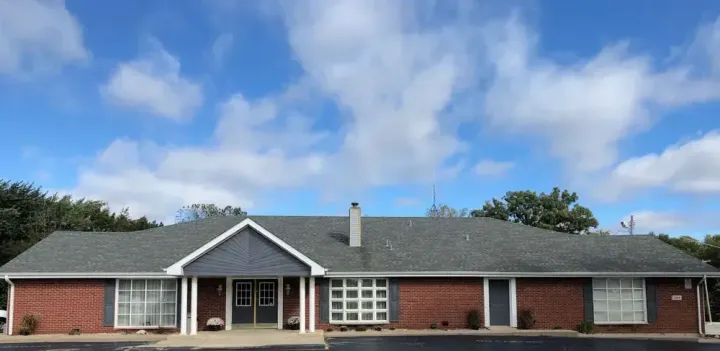 Single-story red brick house with dark roof and white trim under a blue sky