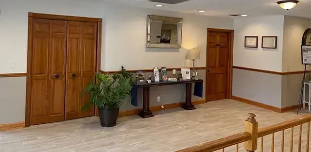 Lobby with wooden cabinets, reception desk, potted plant, and framed wall art in a bright hallway.