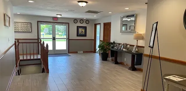 Bright lobby hallway with front doors, wood trim, potted plants, and an easel on the right.
