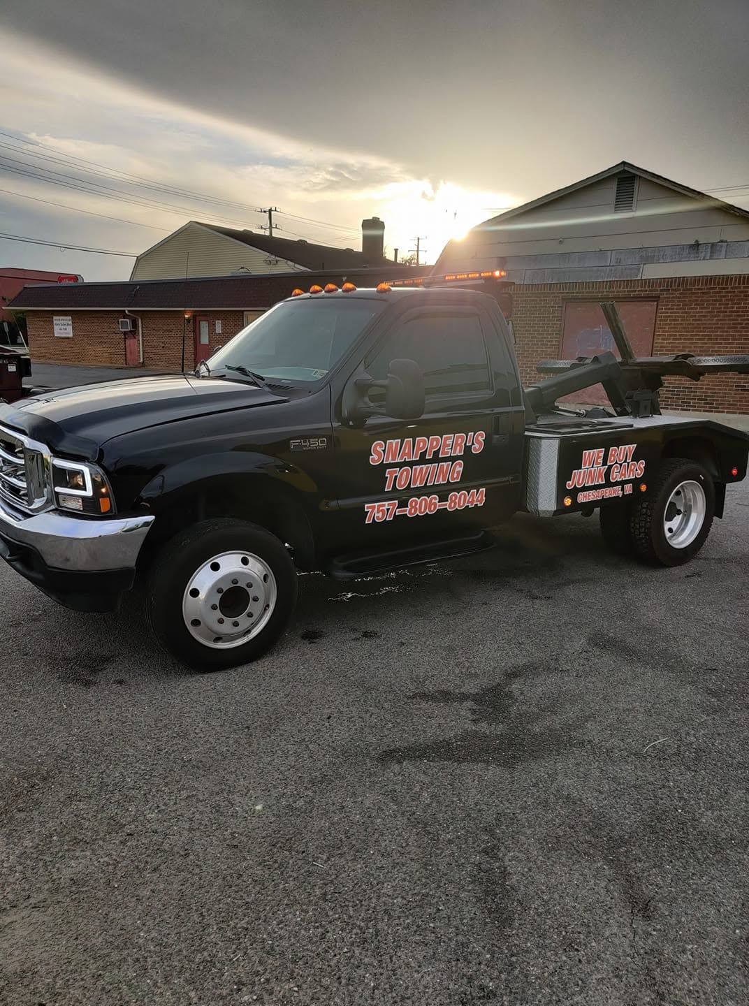 Black pickup truck with pink business signage parked in a driveway at sunset