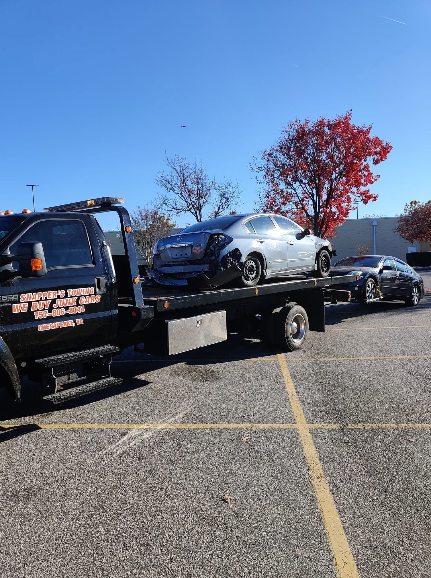 Tow truck carrying a silver car in a parking lot under a clear blue sky