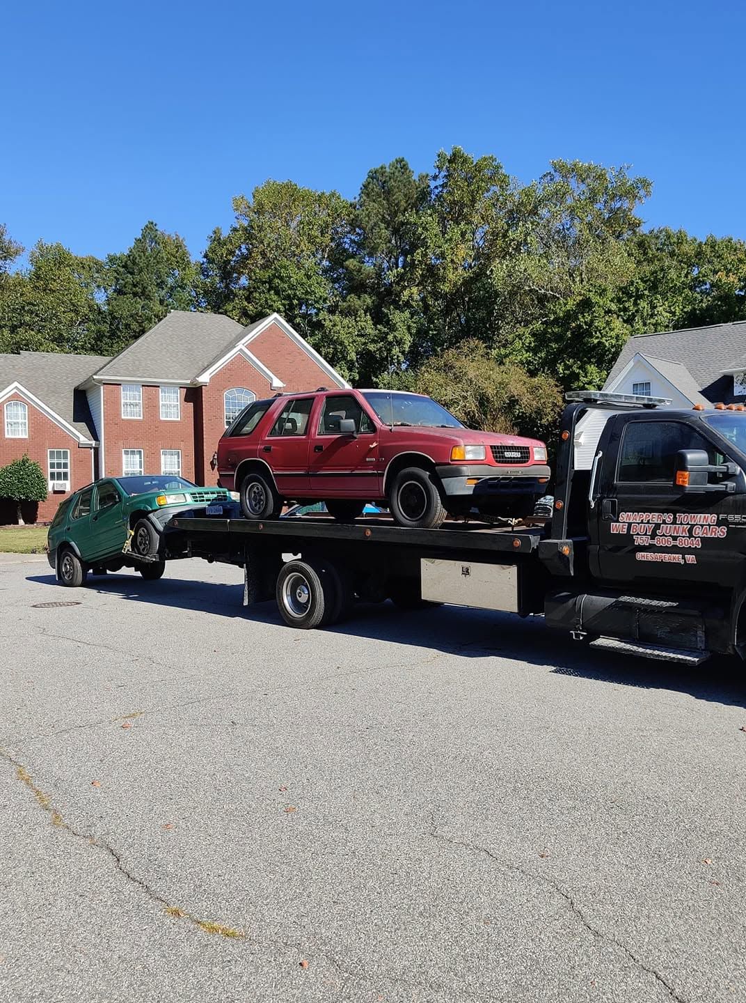 Tow truck hauling a red SUV and green car in a residential neighborhood