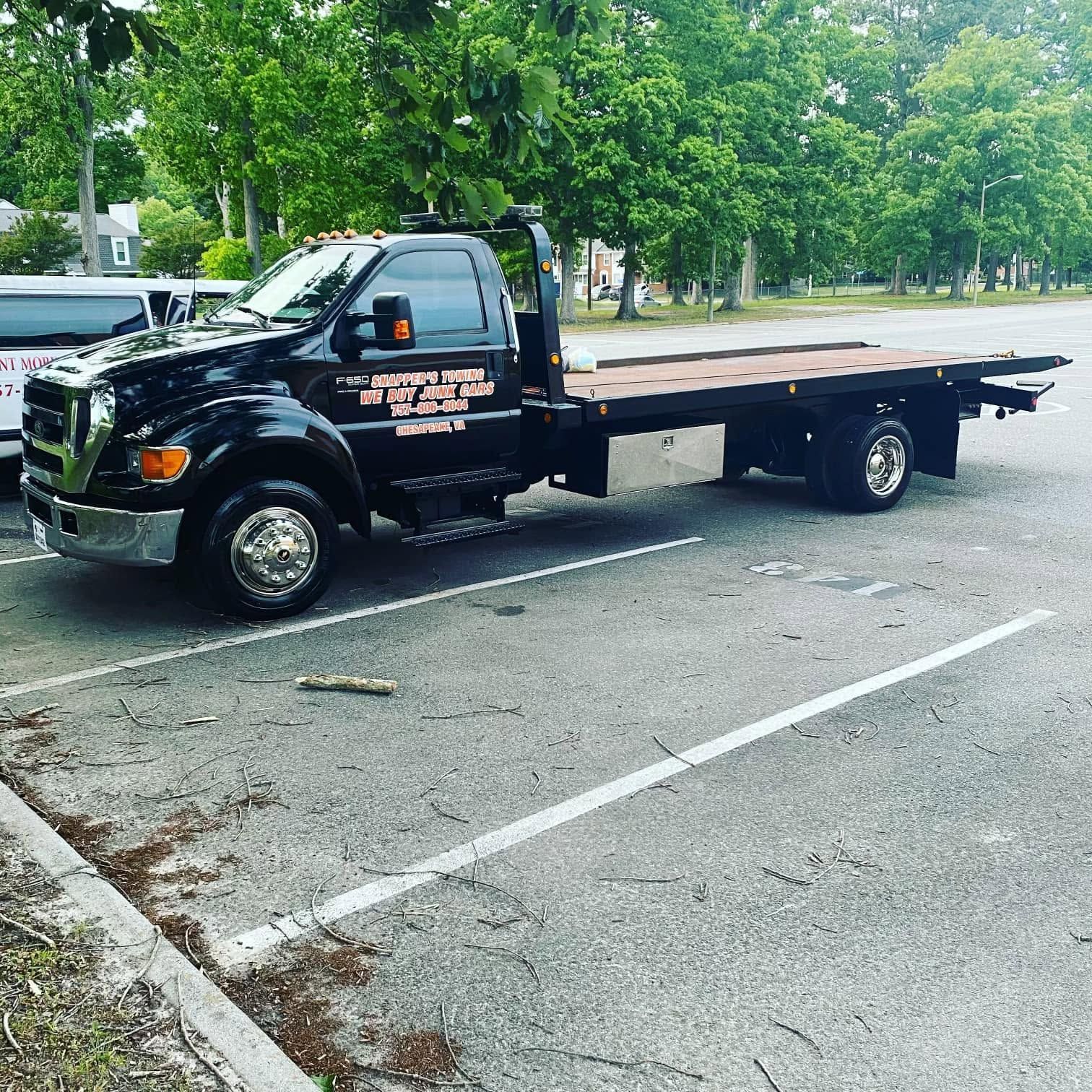 Black flatbed tow truck parked on a tree-lined street beside a curb.
