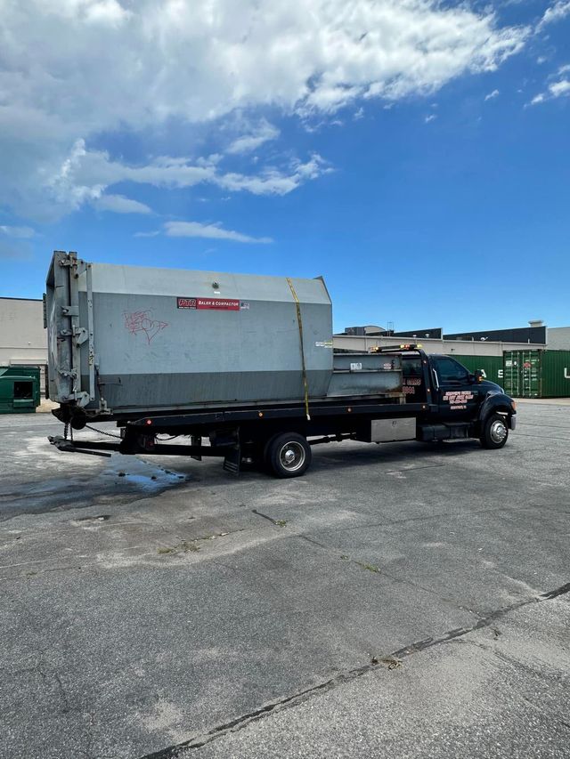 Black garbage truck parked on a gravel lot under a blue sky