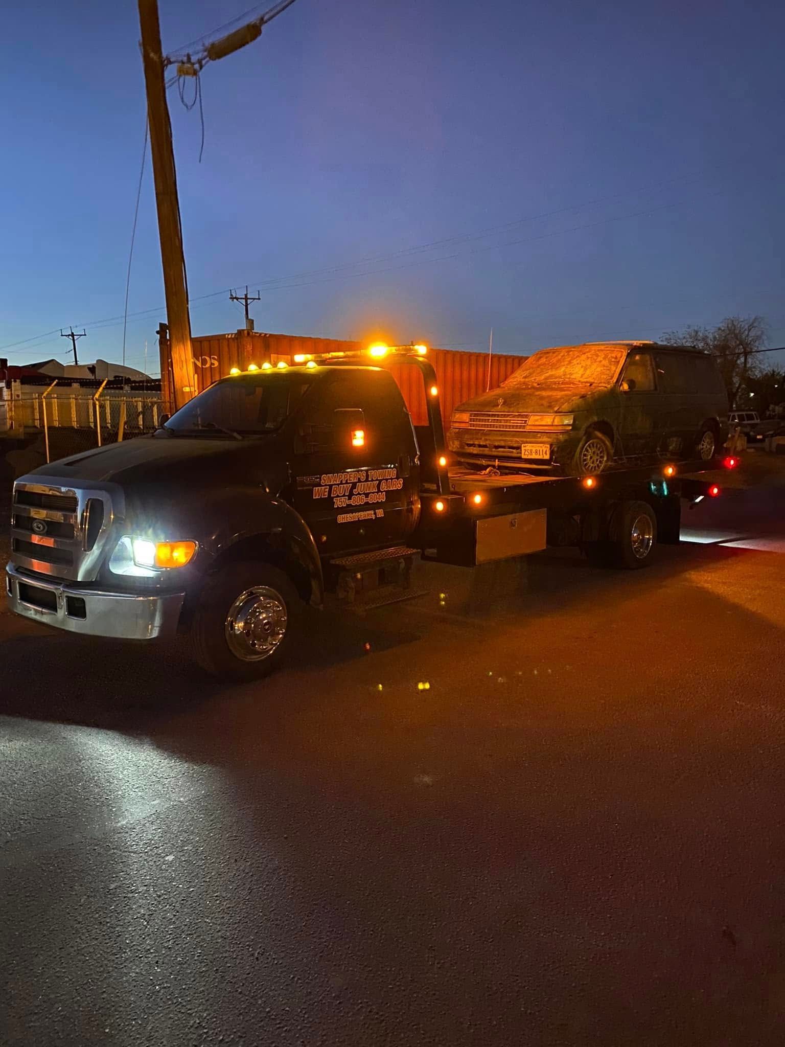 Tow truck with flashing amber lights hauling a car at dusk on a street