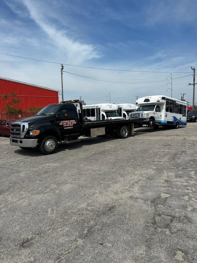 Tow truck carrying a white van in a gravel lot beside a red building under a blue sky