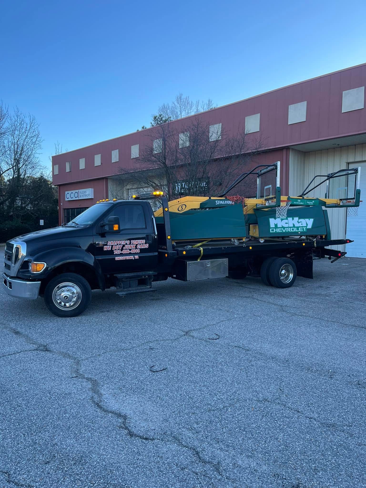 Black dump truck with green trailer parked in front of a brick building on a gravel lot