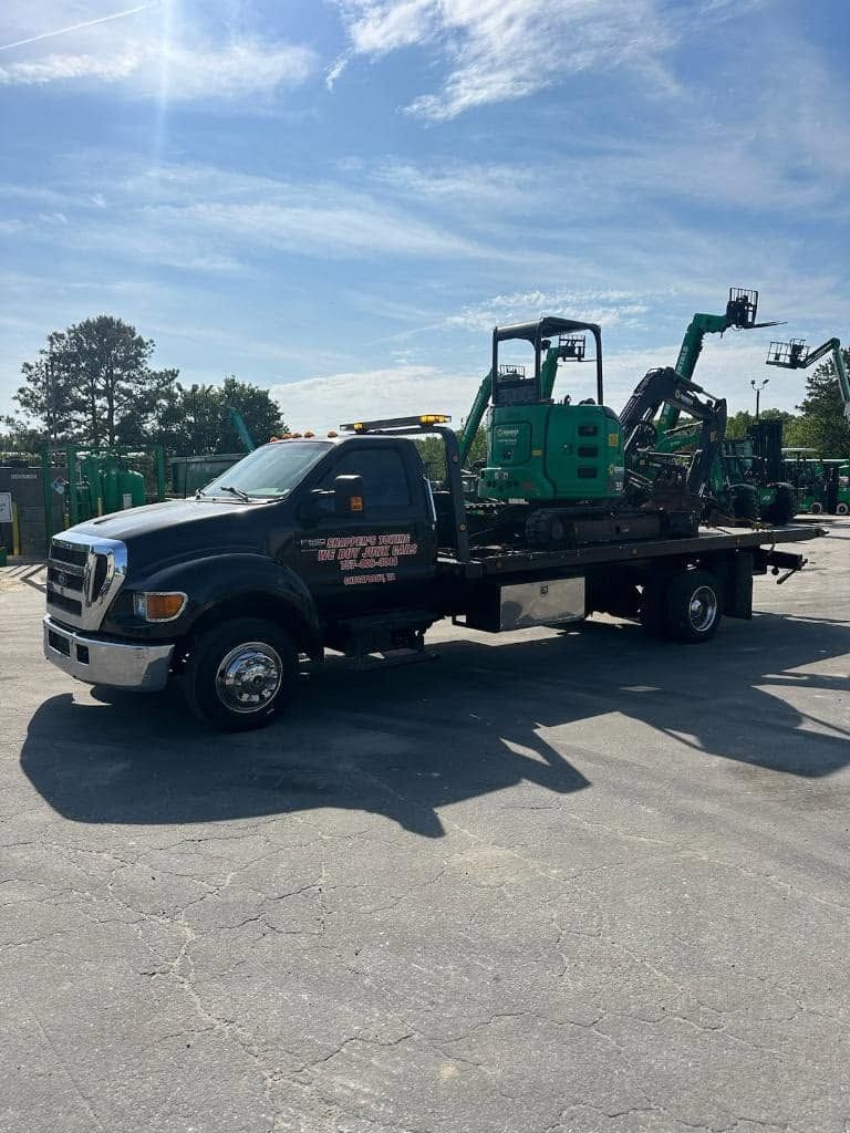 Black flatbed truck hauling a green excavator on a sunny lot